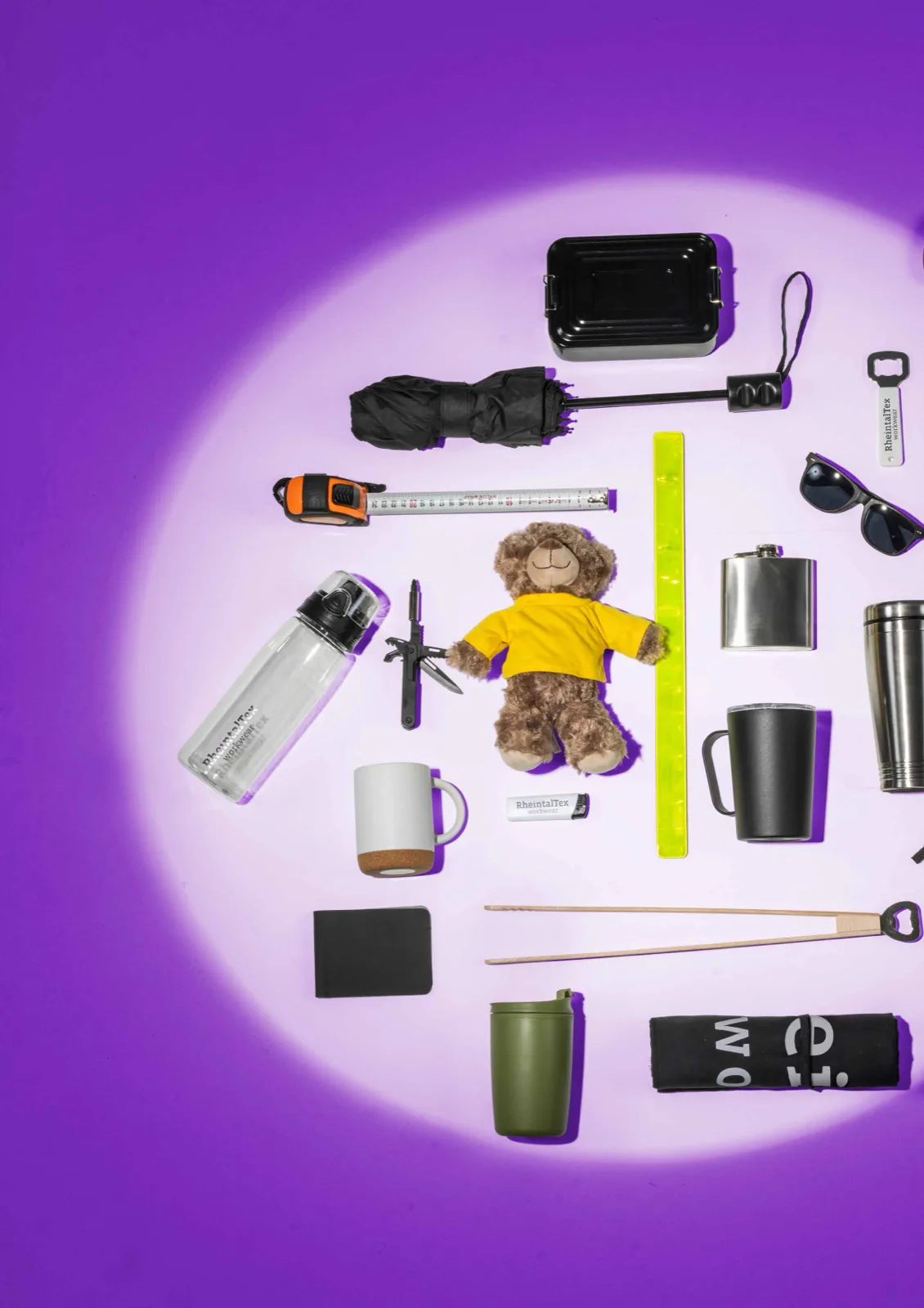 Werbeartikel im violetten Lichtspot: Trinkflasche, Tassen, Teddybär, Multitool, Sonnenbrille und mehr